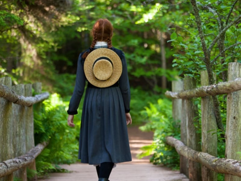 Rear view of Anne of Green Gables walking down a wooden bridge