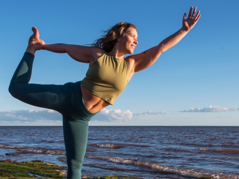 Woman does yoga pose at Canoe Cove beach under a blue sky, PEI