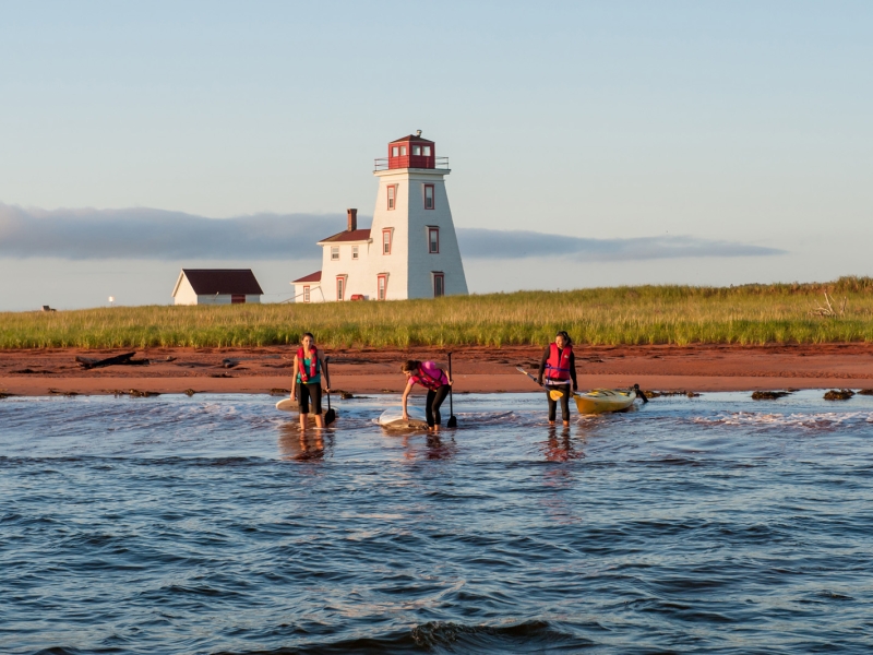 Three persons on paddleboards and kayak near lighthouse