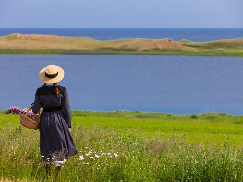 Anne of Green Gables character holding basket of flowers and looking over Lake of Shining Waters