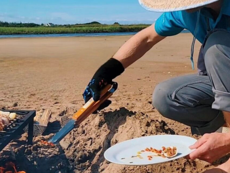 Guide uses tongs to remove PEI seafood from beach fire