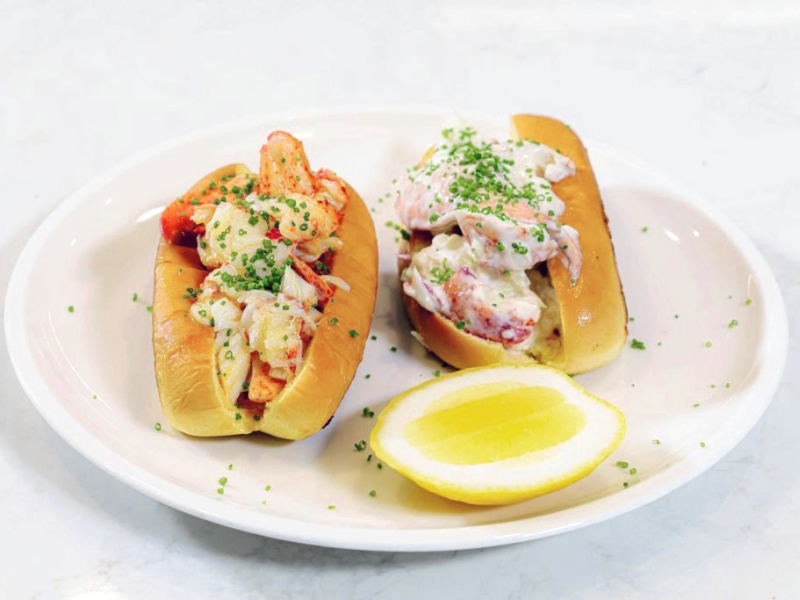 Butter Vs Mayo PEI Lobster Roll Two lobster rolls: One with mayo and one with butter plated with a lemon wedge