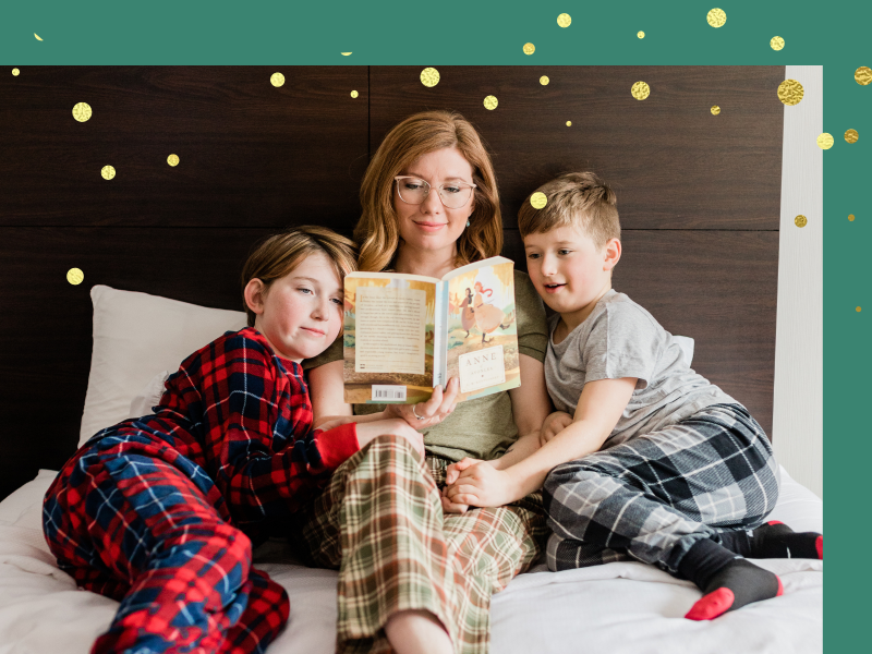 Female adult and two children read a book together in a hotel room