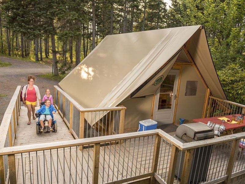 A small child in a wheelchair, an adult and another young child move up ramp to an accessible Parks Canada oTENTik