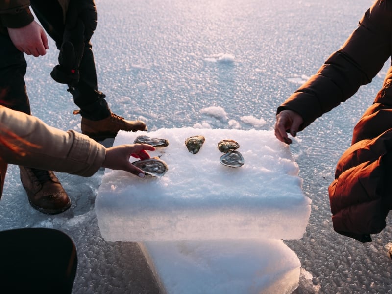 Three people hover over oysters served on ice block outdoors