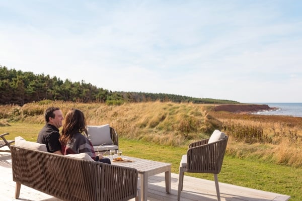 Where to Stay, Prince Edward Island Couple sit on deck overlooking coastal view of red cliffs and water