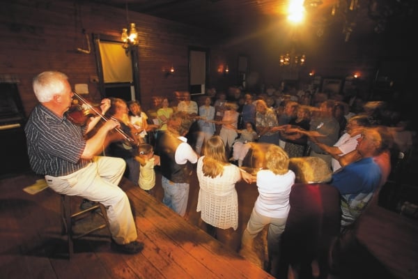 Fiddler in foreground with people doing square dance at Orwell Corner