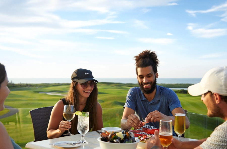 Group enjoying beverages and snacks on outdoor patio at Crowbush with golf course in background