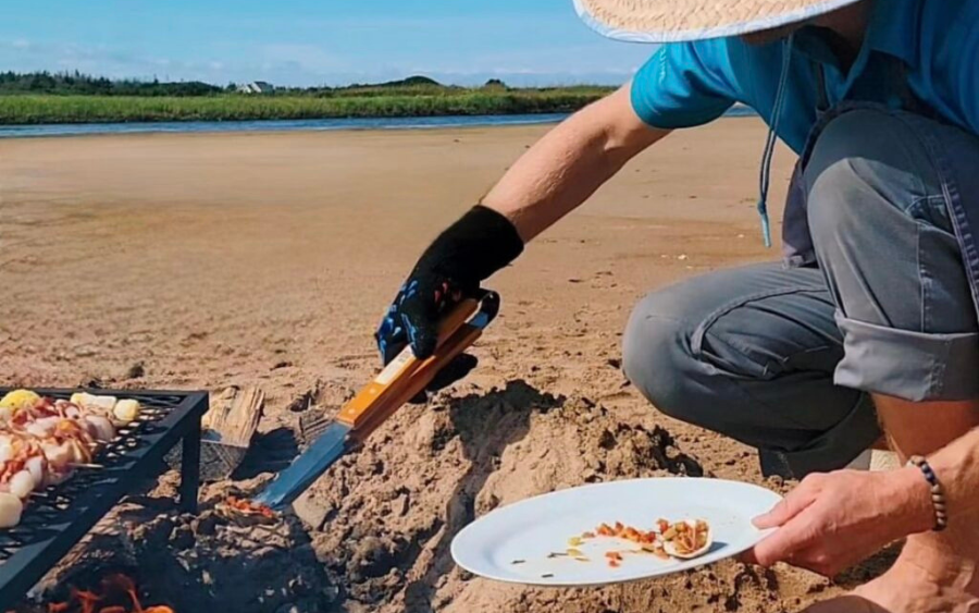 Guide uses tongs to remove PEI seafood from beach fire