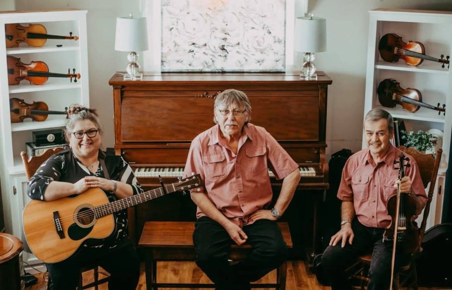 three musicians sitting in front of a piano one holding a guitar one holding a fiddle