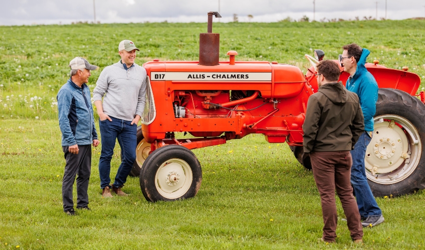 Two members of Roberts family chat with visitors while standing next to antique tractor near a potato field