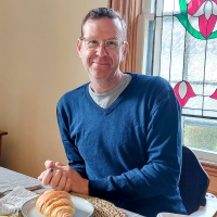 Image of Rod Weatherbie sitting at a dining room table with a crossaint on a plate