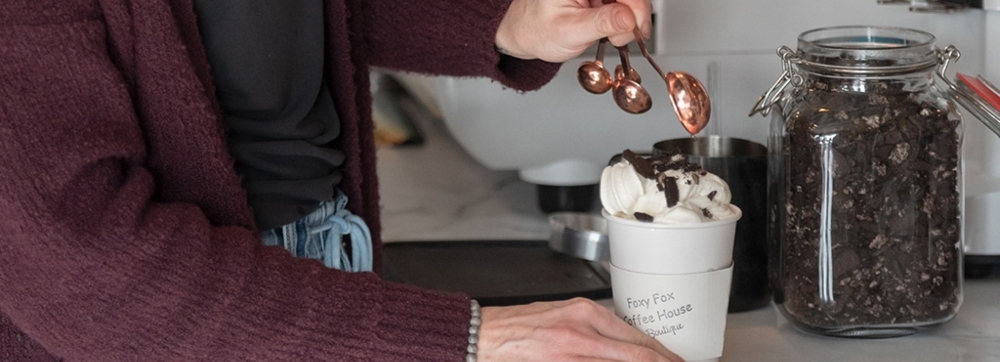 Person making hot chocolate next to expresso machine at Foxy Fox Coffee House & Boutique